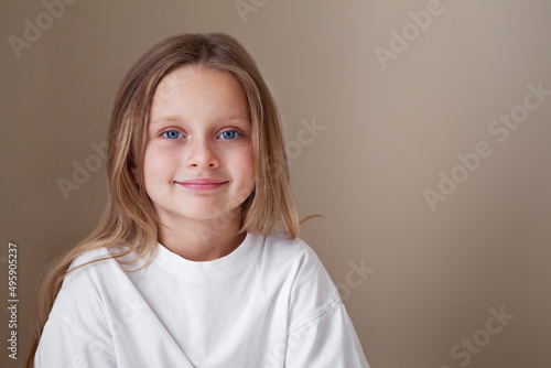 Pretty little girl blue eyes and long blonde hair wears white shirt isolated beige background. Caucasian beautiful fashion child model, natural lighting