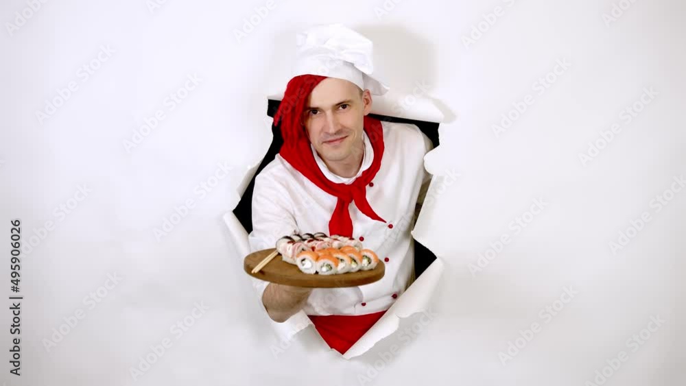 Young man dressed as chef holding wooden board with sushi rolls. Male cook with appetizing sushi rolls in hole of white background. Concept of fast food and takeaway. Young man dressed as chef holding wooden board with sushi rolls. Male cook with appetizing sushi rolls in hole of white background. Concept of fast food and takeaway.