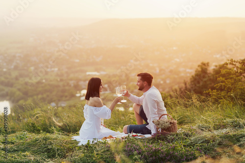 Couple in love on a white plaid take a picnic against the backdrop of a sunset in the mountains. Romantic time. Beautiful couple is enjoying picnic time at sunset. Copy space.