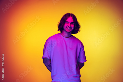 Portrait of young man, student in casual clothes isolated on orange background in purple neon light. Concept of emotions, beauty, fashion © master1305