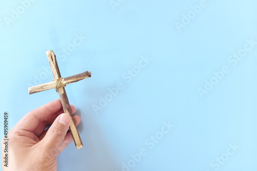 Top view of hand holding wooden cross crucifix with copy space in blue background. Catholicism, Christianity, Thanksgiving, Catholic and Christian faith concept.