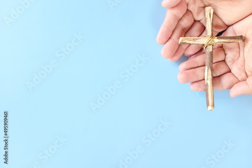 Top view of hand holding wooden cross crucifix with copy space in blue background. Catholicism, Christianity, Thanksgiving, Catholic and Christian faith concept.