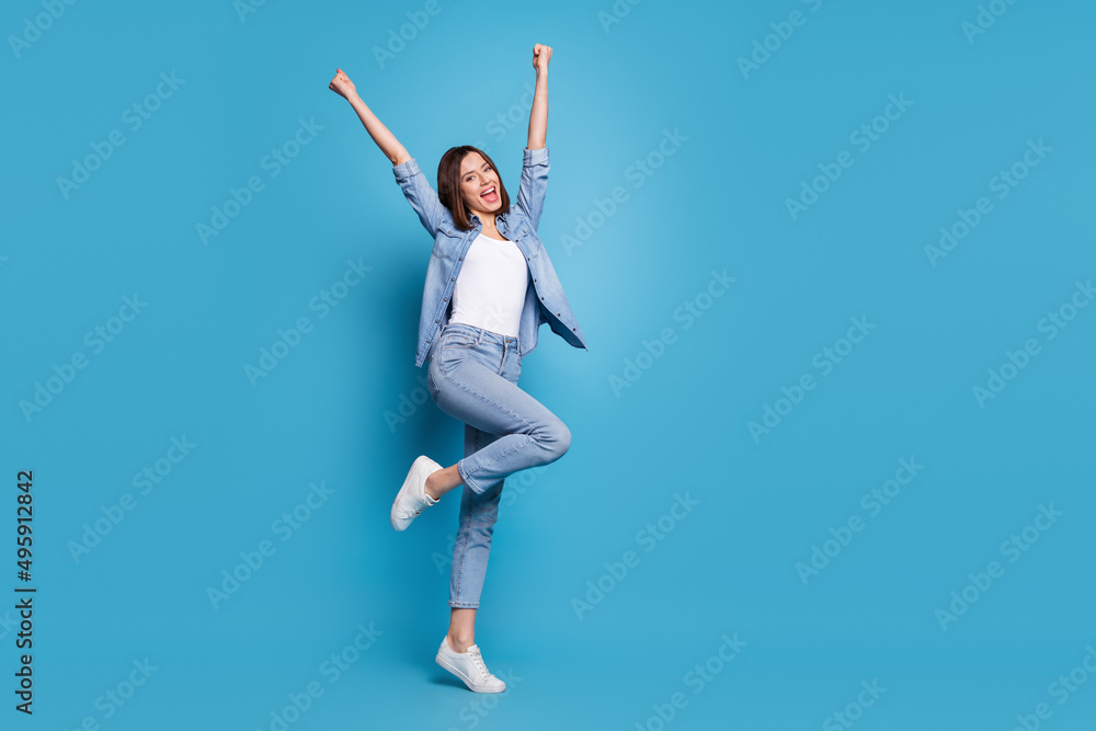 Photo of lucky excited woman wear jeans shirt screaming rising fists empty space isolated blue color background Photo of lucky excited woman wear jeans shirt screaming rising fists empty space isolated blue color background