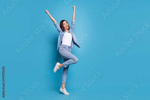 Photo of lucky excited woman wear jeans shirt screaming rising fists empty space isolated blue color background