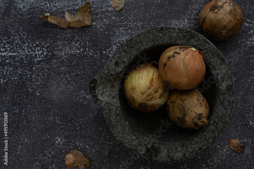 Onions in a mortar bowl and beside the bowl, placed on a coloured background. Still life food photography