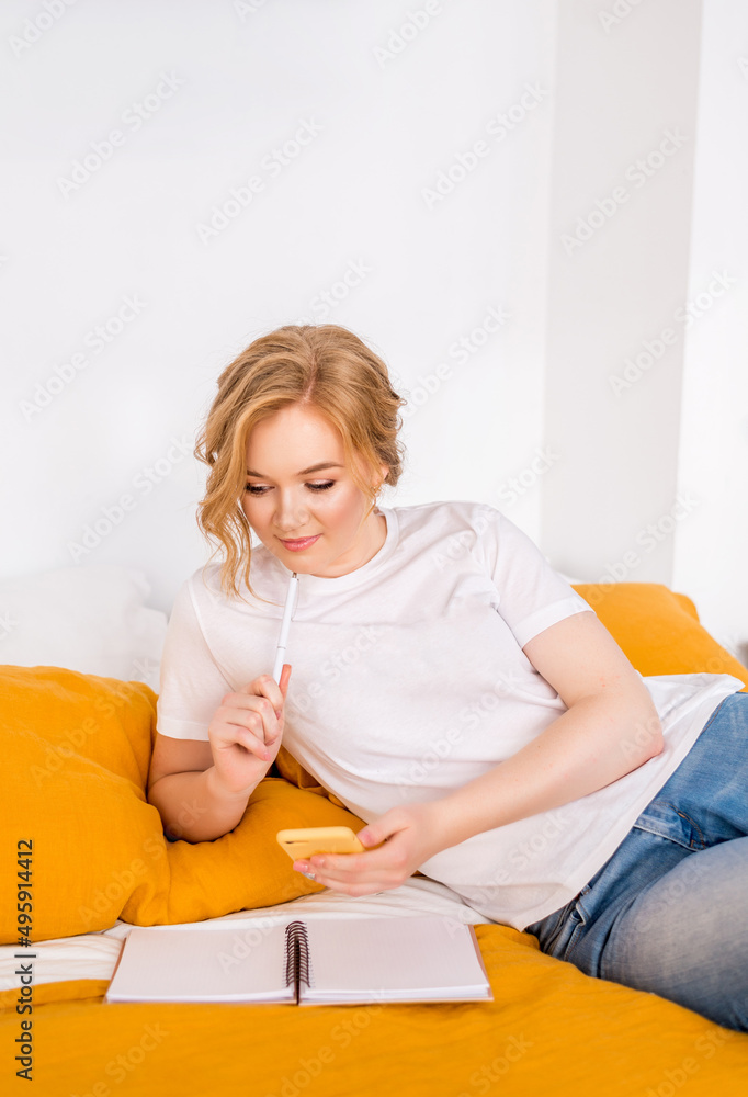 girl is lying on the bed. A freelance woman with a phone and a notebook at home girl is lying on the bed. A freelance woman with a phone and a notebook at home