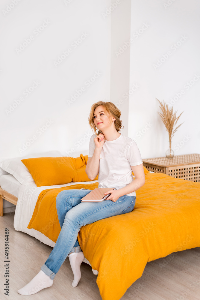 thoughtful girl is sitting on the bed. A female freelancer with a notepad for writing thoughtful girl is sitting on the bed. A female freelancer with a notepad for writing
