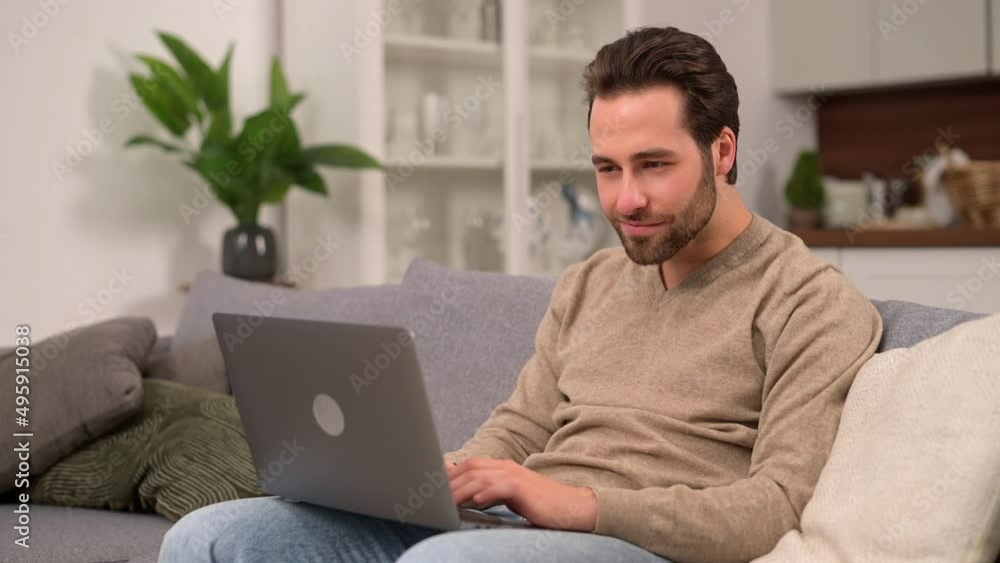 Cheerful caucasian man wearing casual wear sitting on sofa and using laptop at modern home office. Serene male entrepreneur typing on keyboard and closed laptop up after successful working day done Cheerful caucasian man wearing casual wear sitting on sofa and using laptop at modern home office. Serene male entrepreneur typing on keyboard and closed laptop up after successful working day done