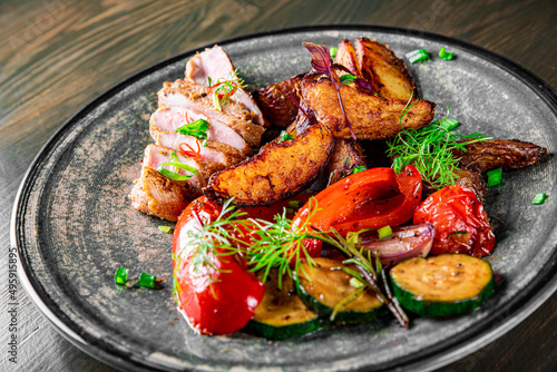 fried meat with potatoes, pepper, tomatoes, herbs and spices in plate
