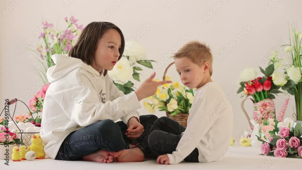 Cute stylish toddler child and older brother, boys with white shirt, playing with eggs and chocolate bunny on Easter decoration, studio shot Cute stylish toddler child and older brother, boys with white shirt, playing with eggs and chocolate bunny on Easter decoration, studio shot