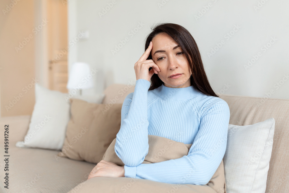 Frustrated Asian lady sitting on sofa, cuddling pillow, looking away at window. Lost in thoughts unhappy stressed woman regretting of wrong decision, spending time alone in living room. Frustrated Asian lady sitting on sofa, cuddling pillow, looking away at window. Lost in thoughts unhappy stressed woman regretting of wrong decision, spending time alone in living room.