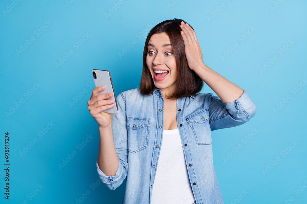 Photo of funny shocked lady dressed denim shirt laughing reading gadget empty space isolated blue color background Photo of funny shocked lady dressed denim shirt laughing reading gadget empty space isolated blue color background