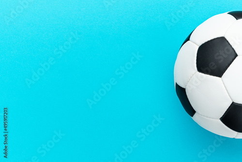 Minimalist flat lay image of leather football ball over blue turquoise background with copy space and right side composition. Top view photo of white and black soccer ball as football concept.