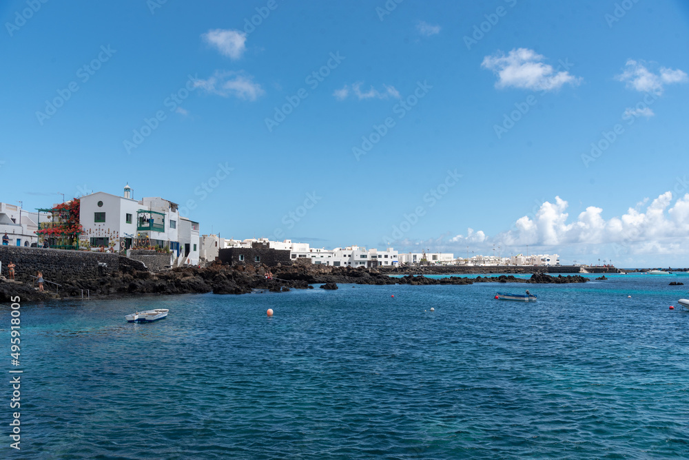 Vista panorámica del pueblo Punta Mujeres en Lanzarote con sus tradicionales casas blancas, frente a un mar turquesa y cristalino con pequeñas barcas un día soleado de verano en las Islas Canarias.