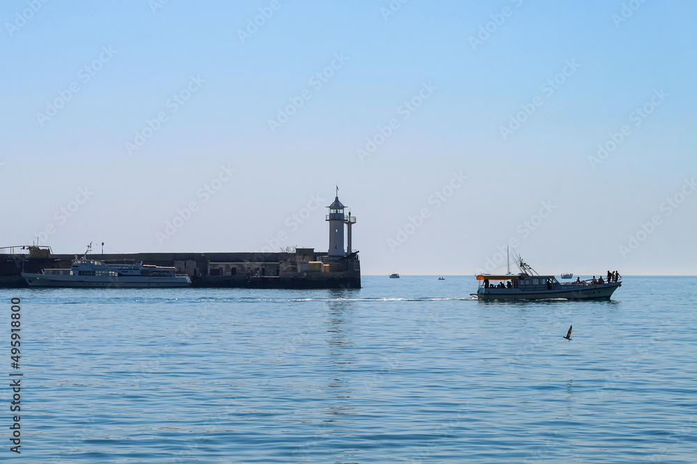 A tranquil seascape. Small pleasure boats on the background of the white tower of the old lighthouse. Yalta, Crimea.