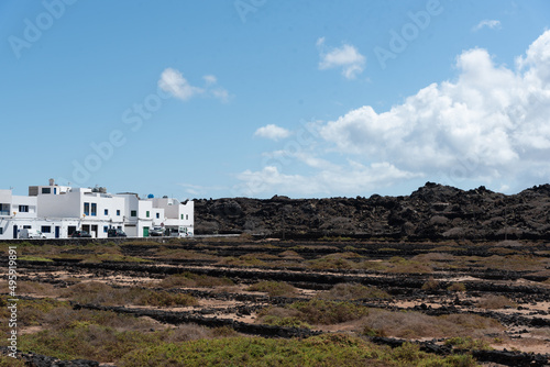 Salinas de Lanzarote con el pueblo Orzola al fondo con la arquitectura tradicional de casas blancas en un día soleado con el cielo azul. Recursos turísticos naturales y culturales de islas Canarias