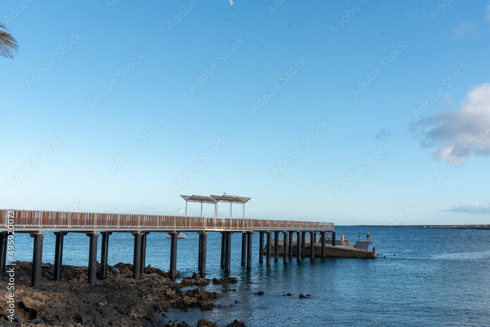 Paisaje costero en Lanzarote Islas Canarias, Muelle la Garita en Arrieta que se adentra en el mar turquesa durante un día de verano soleado y con el cielo despejado. Recursos turísticos naturales.