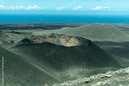 Paisaje desértico del Parque Nacional de Timanfaya en Lanzarote, con dos grandes volcanes inactivos en el centro y un gran cráter un día soleado con cielo azul. Recursos turísticos naturales.
