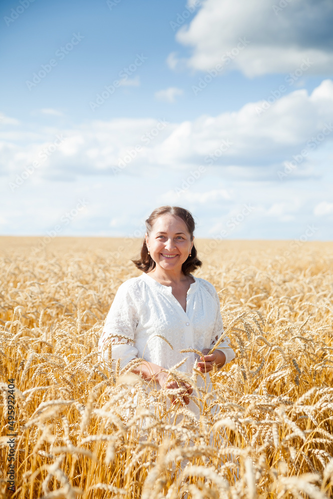 Elderly woman in white walking through wheat field.