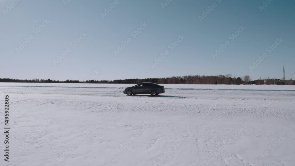 The car drives along the road among the snow-covered fields in winter, aerial photography of the movement of the car on the winter road The car drives along the road among the snow-covered fields in winter, aerial photography of the movement of the car on the winter road