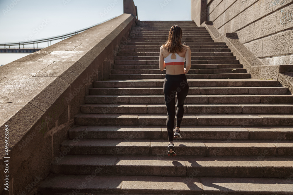 Sportive lady in modern tracksuit runs up stone stairs on city waterfront Sportive lady in modern tracksuit runs up stone stairs on city waterfront