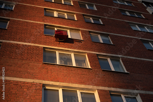 Red air conditioner on the facade of a brick building under the rays of the setting sun