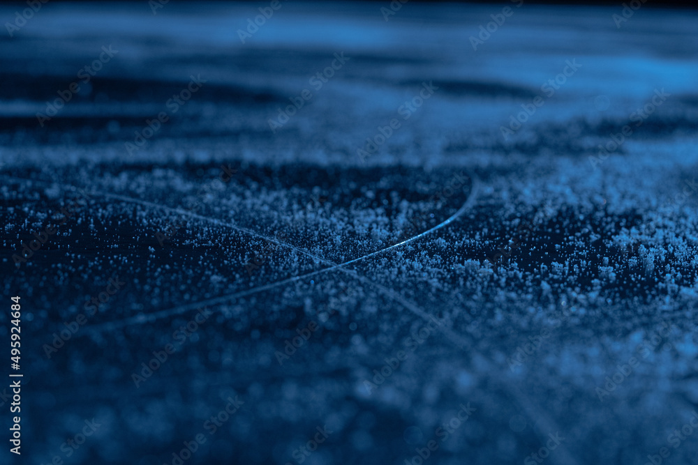 Ice background and texture with scratches from skating and hockey. Ice rink floor, detail of textured ice background with snow and crystals in blue light. Empty ice rink close up. Ice background and texture with scratches from skating and hockey. Ice rink floor, detail of textured ice background with snow and crystals in blue light. Empty ice rink close up.