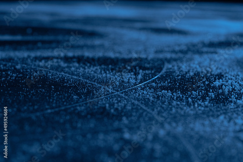 Ice background and texture with scratches from skating and hockey. Ice rink floor, detail of textured ice background with snow and crystals in blue light. Empty ice rink close up. © kinomaster