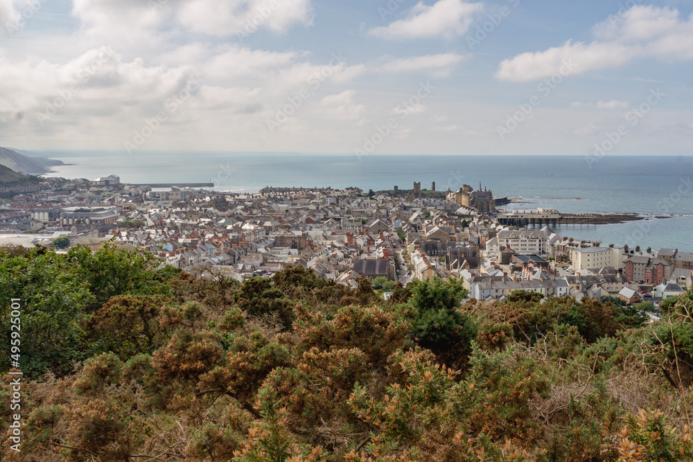 A view over the town of Aberystwyth from the hills to the north of the town. Taken on a sunny autumn day with gorse bushes in the foreground and calm flat sea.
