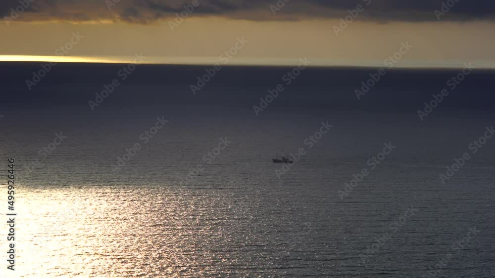 A small fishing ship sails in the sea at sunset on a cloudy rainy day under heavy clouds, top view A small fishing ship sails in the sea at sunset on a cloudy rainy day under heavy clouds, top view