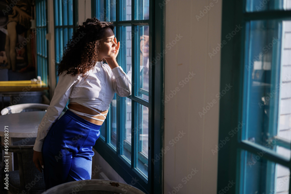 Serious curly girl in cafe, thoughful. Woman in white blouse and blue trousers closed and distrustful in sun light