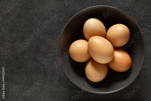 Eggs chicken whole beige in bowl, on dark background, top view, space to copy text.