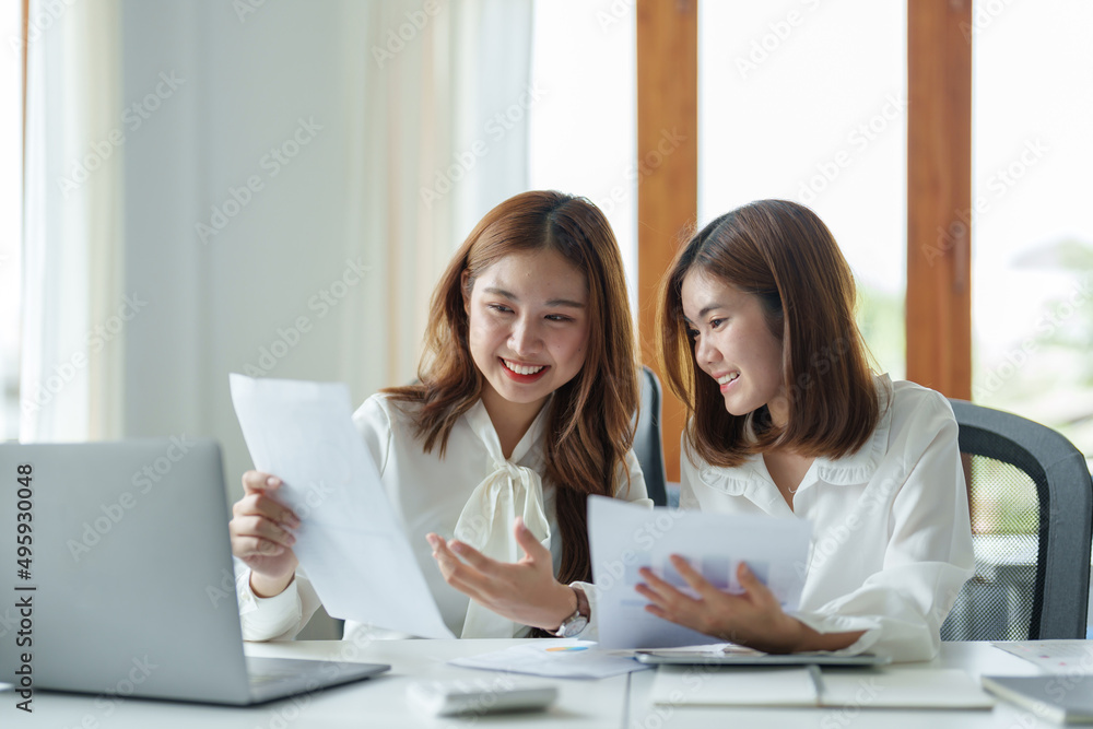 Two colleagues or students, asian girl working for financial paperwork while sitting at workplace discussing about job or education Two colleagues or students, asian girl working for financial paperwork while sitting at workplace discussing about job or education