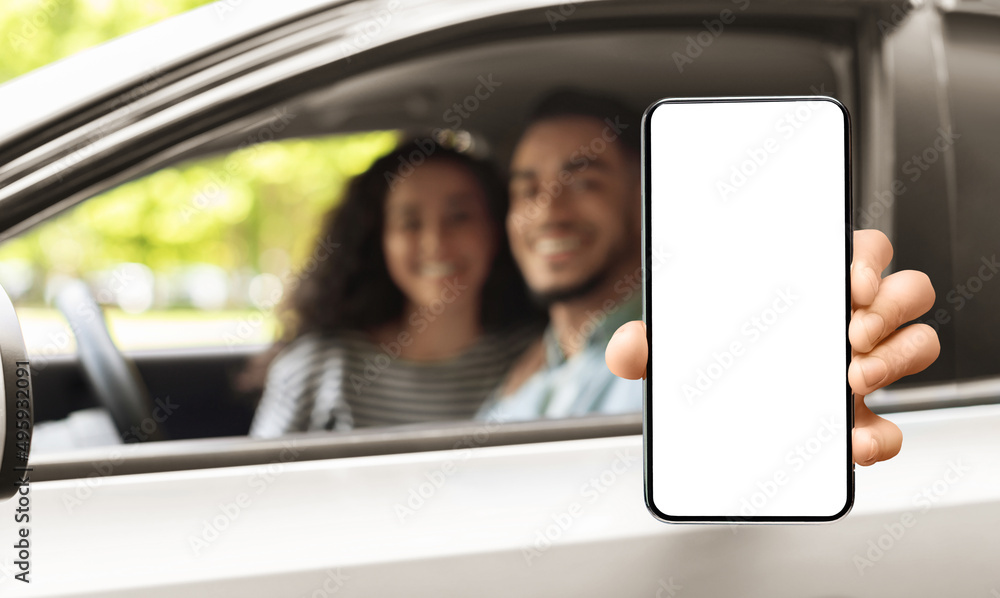 Car Rental App. Arab Couple Showing Blank Smartphone While Sitting In Auto Car Rental App. Arab Couple Showing Blank Smartphone While Sitting In Auto