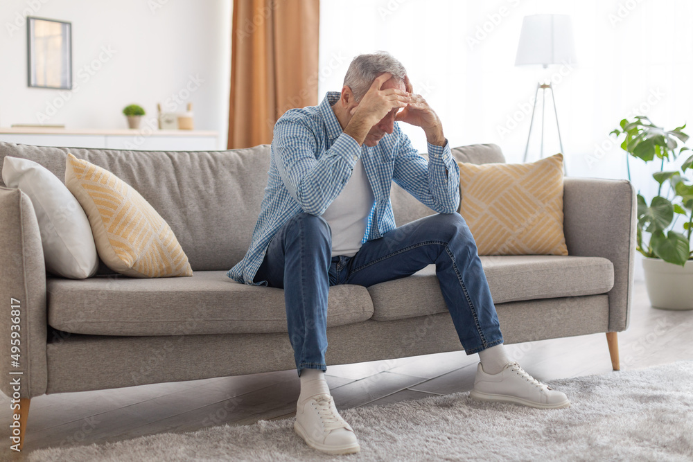 Stressed mature man sitting on couch grabbing head