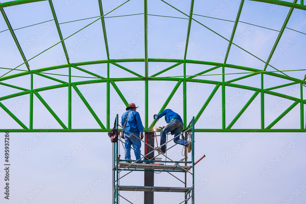 Asian foreman and construction worker on scaffolding are working to build metal roof structure of industrial building in construction site