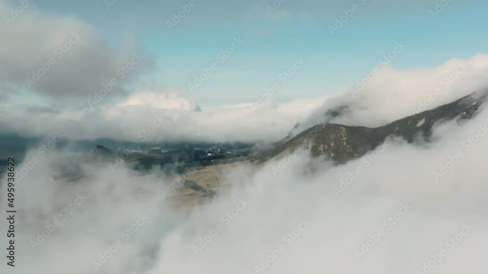 Aerial view of the suburbs in the mountains through low cloud cover. Above the clouds, a daytime flight above the clouds with a view of the city in the mountains Aerial view of the suburbs in the mountains through low cloud cover. Above the clouds, a daytime flight above the clouds with a view of the city in the mountains