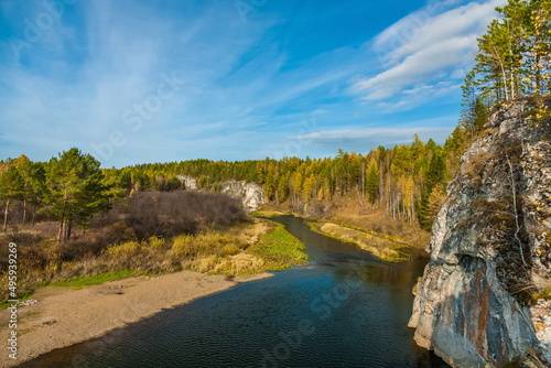 Autumn landscape with river, rock, trees, grass and blue sky