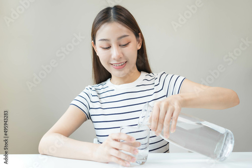 Happy beautiful, thirsty asian young woman, girl drinking, hand in holding, pouring water from jug into transparent glass from pitcher for hydration of body. Health care, healthy lifestyle concept.