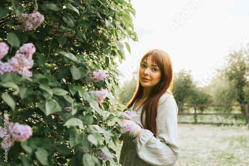 young woman plus size model stands in park next to blooming lilac tree, concept of spring