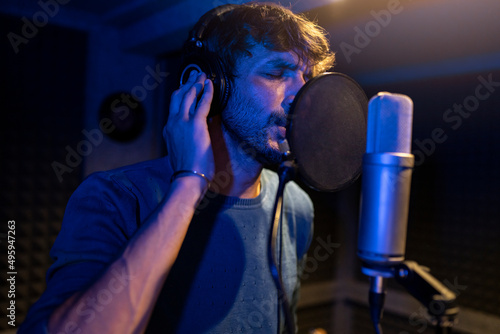man recording song with microphone in neon light recording studio