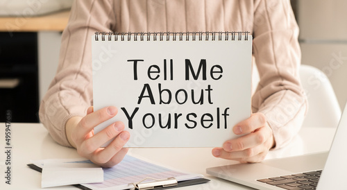 Closeup on femal holding a card with TELL ME ABOUT YOURSELF message, business concept image with soft focus background