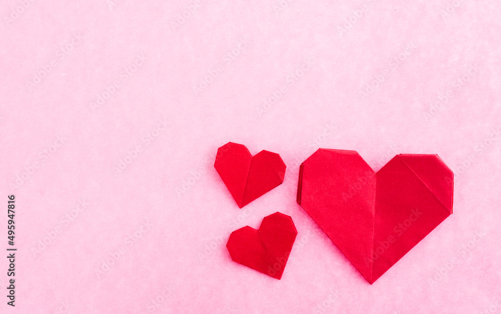 Red origami hearts on pink background.