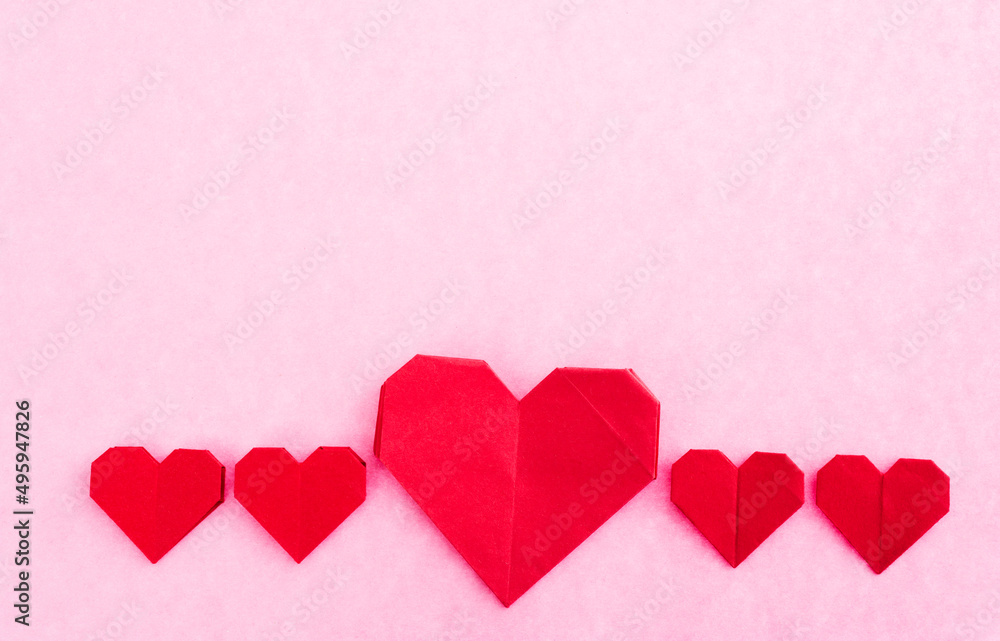 Red origami hearts on pink background