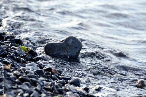 Heart shape stone against background of beach. Summer sunny day. Love, wedding and Valentine day concept. Finding beautiful and interesting stones. Beach vacation. 