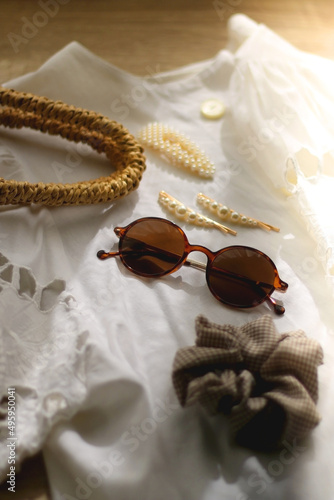 White linen lace shirt, round straw bag, sunglasses and cute hair accessories on wooden background. Selective focus.