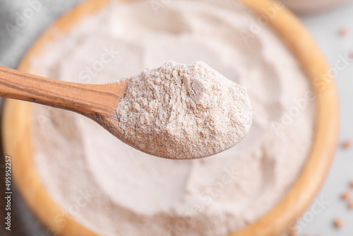 Buckwheat flour in a wooden bowl with wooden spoon, close up, top view, selective focus. Alternative flour, gluten free flour, healthy nutrition