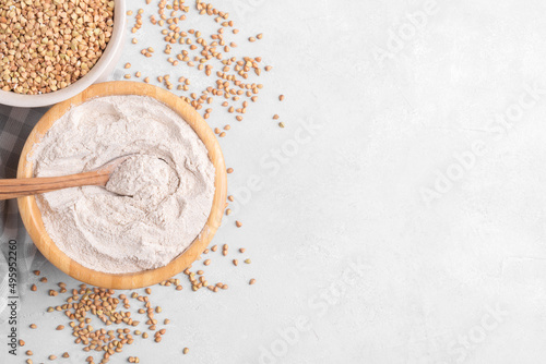 Buckwheat flour in a wooden bowl with wooden spoon and raw green buckwheat grain in a bowl on light grey concrete background, close up top view. Alternative flour, gluten free flour, healthy nutrition photo
