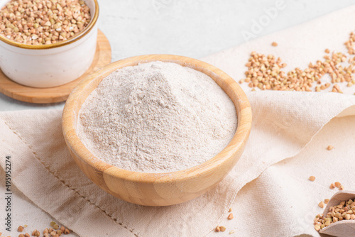 Buckwheat flour in a wooden bowl and raw green buckwheat grain on cotton napkin on light grey table stone background, close up. Alternative flour, gluten free flour, healthy nutrition