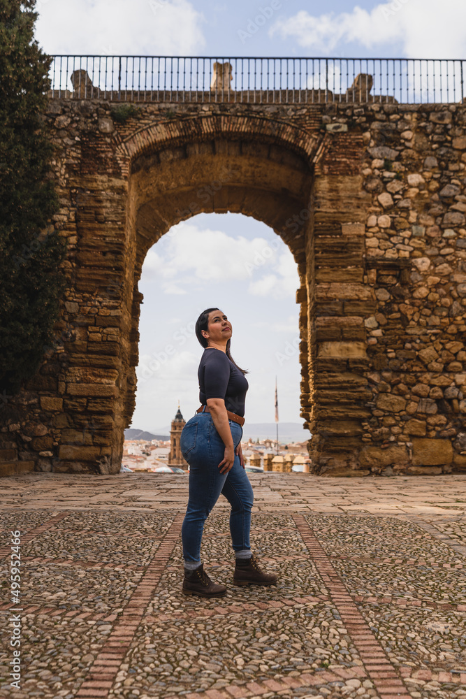 Chica joven guapa saltando frente a puerta de muro en pueblo blanco andaluz